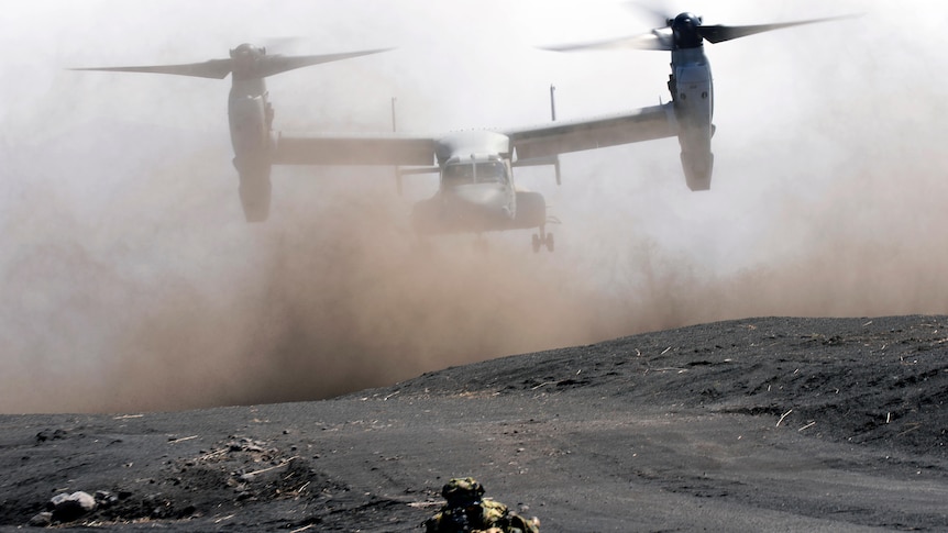 An MV-22 takes off the dusty ground in a military drill