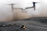 An MV-22 takes off the dusty ground in a military drill