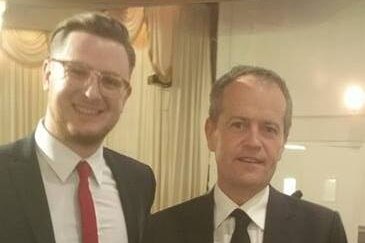 Tim Griffin, wearing a red skinny tie and glasses, smiles next to Bill Shorten. There is quite a height difference.