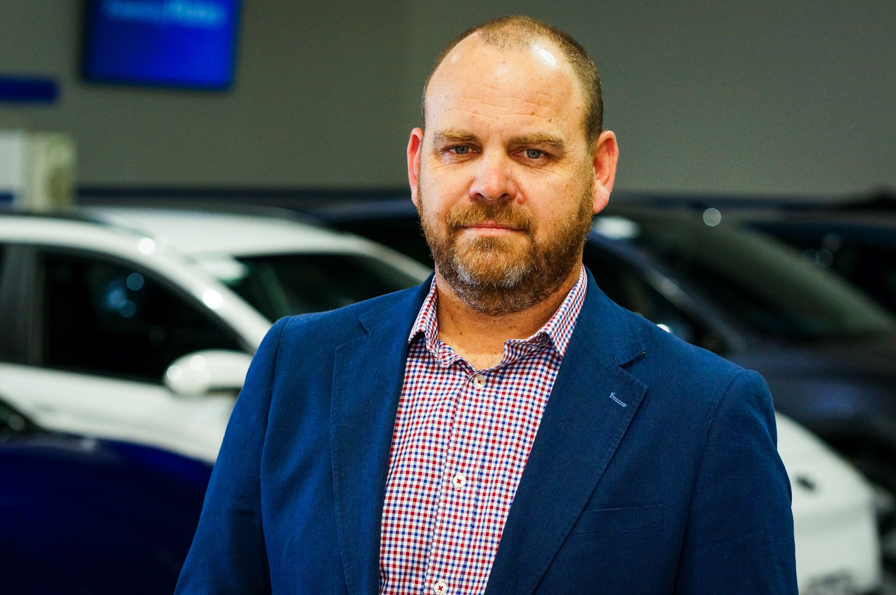 A man in a button-up shirt and blazer stands in front of a row of electric vehicles.