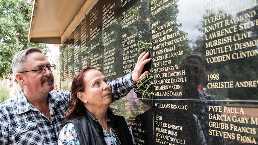 A man and woman standing in front of an honour roll for mine workers who have died on the job.