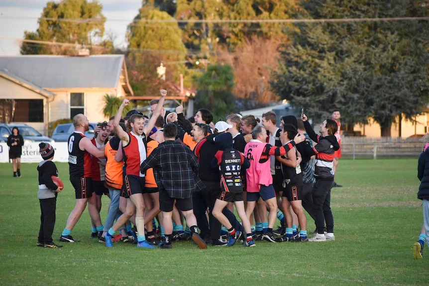 Players in football jerseys and shorts run into a huddle in the middle of a football oval.