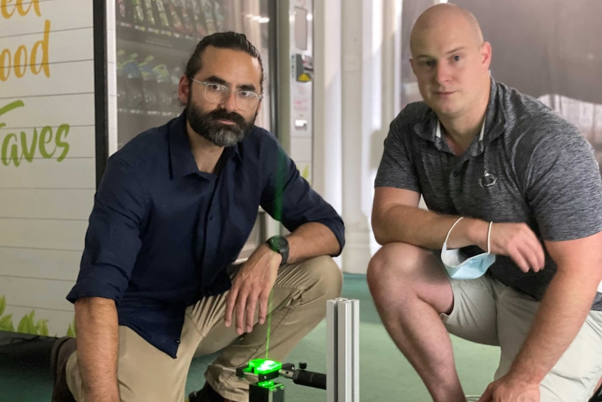 Two men kneeling down next to a green laser.