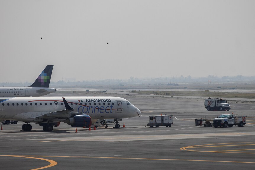 Aircraft and vehicles sit on airport tarmac under grey and hazy skies.
