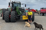 Young boy sits on the front of a tractor, man in hi-vis shirt stands next to him.
