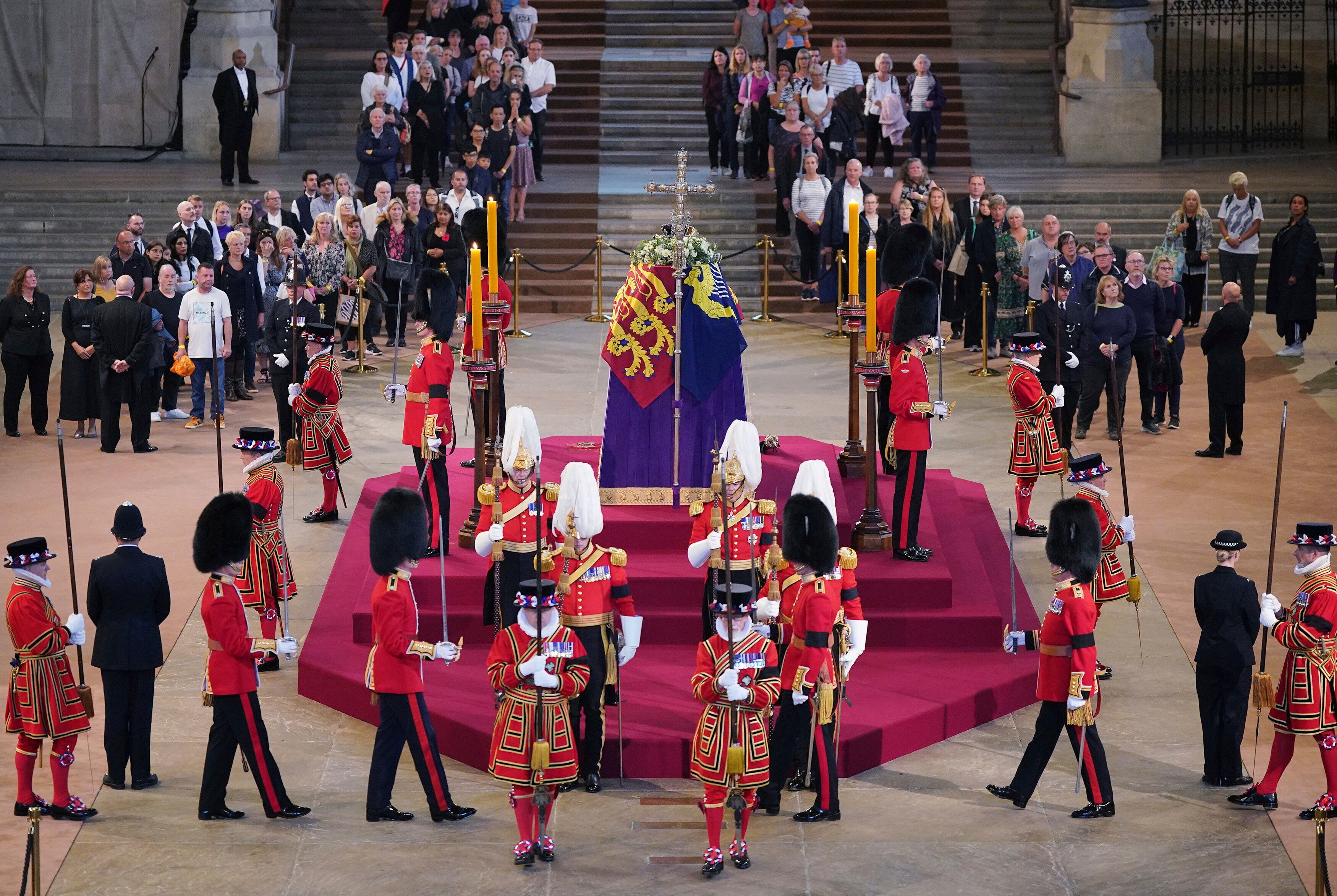 People in queues watch royal guards marching around and standing by the Queen's coffin.