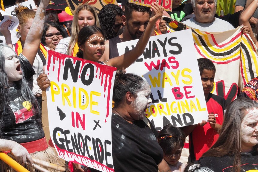Aboriginal people hold signs and placards, with red black and yellow text