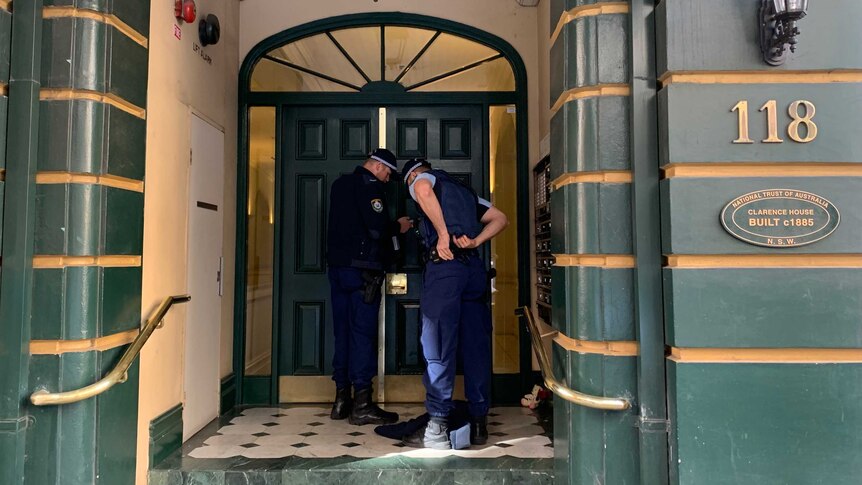 Two NSW police officers stand by the door of a Sydney apartment where a woman was found dead.