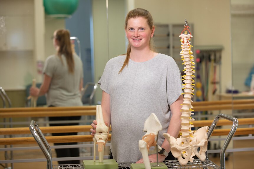 A woman stands behind models of bones.