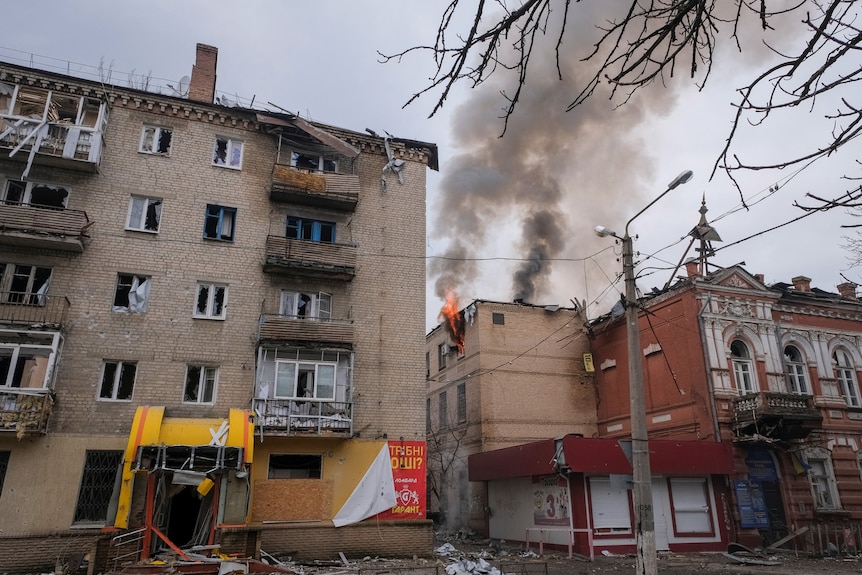 A general view shows buildings with shattered windows and smoke billowing.