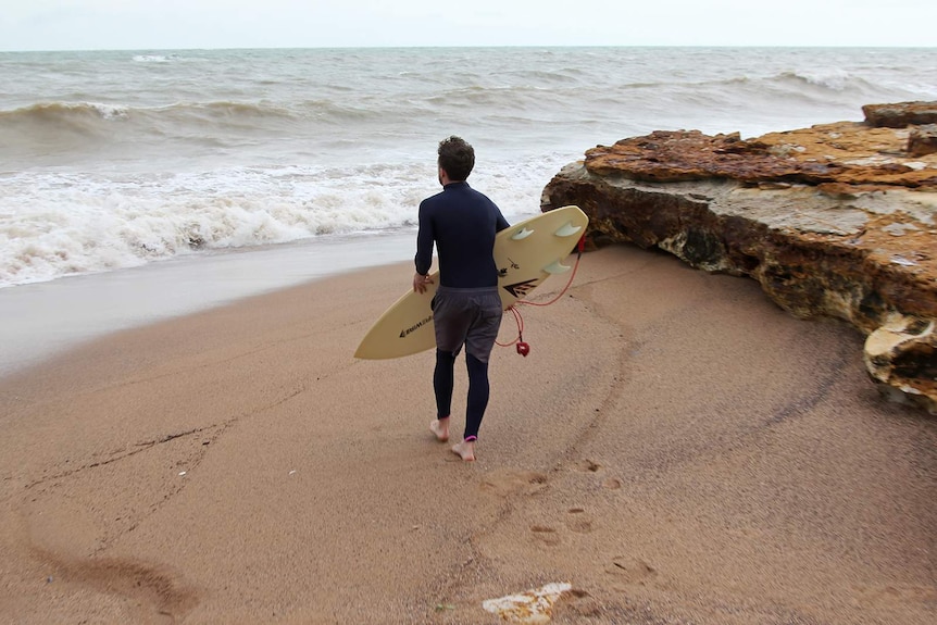Surfer Sam Carmody heads into the choppy Darwin water, surfboard in tow.