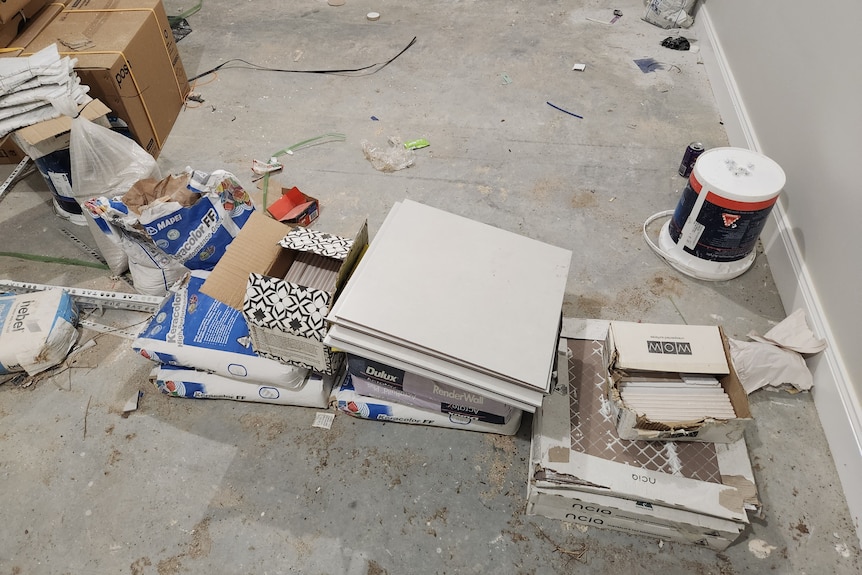 a pile of tiles and building supplies stacked on an unsealed concrete floor