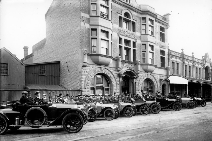 A black and white image of a dozen travelling salesmen in cars outside the CTA headquarters in 1914.