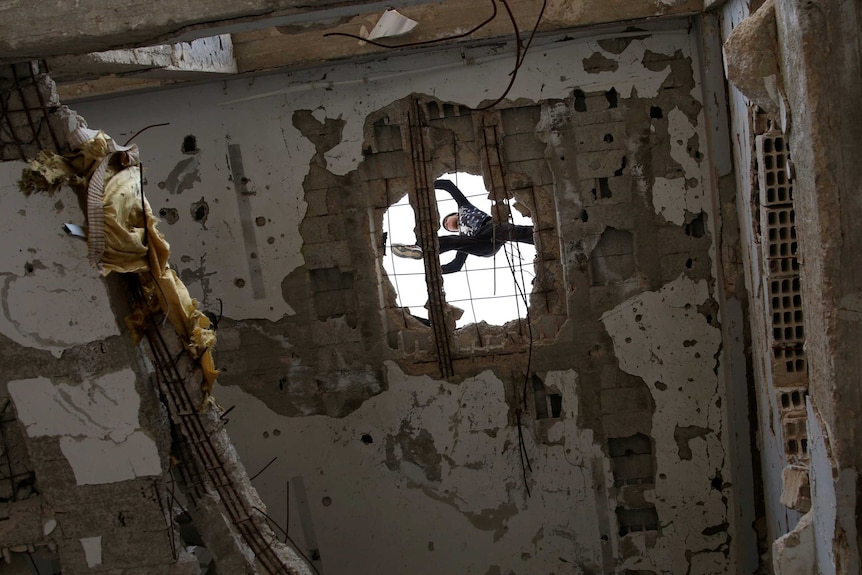 A Syrian man jumps over a hole in the roof of a damaged building in the Syrian city of Inkhil.