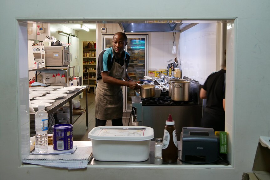 A middle aged man leans over pots and plates in a kitchen.