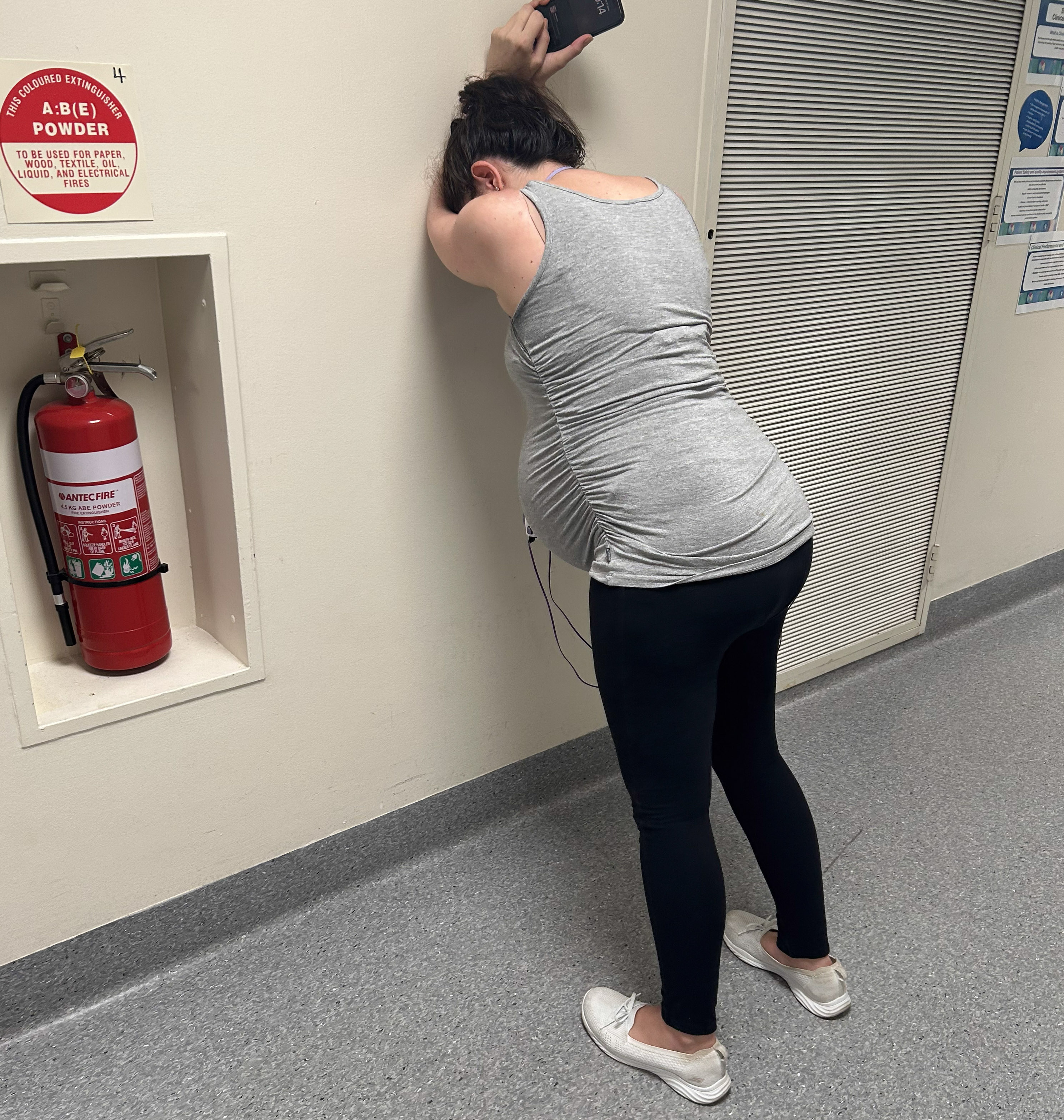 A woman in labour leans against the wall in a hospital corridor.
