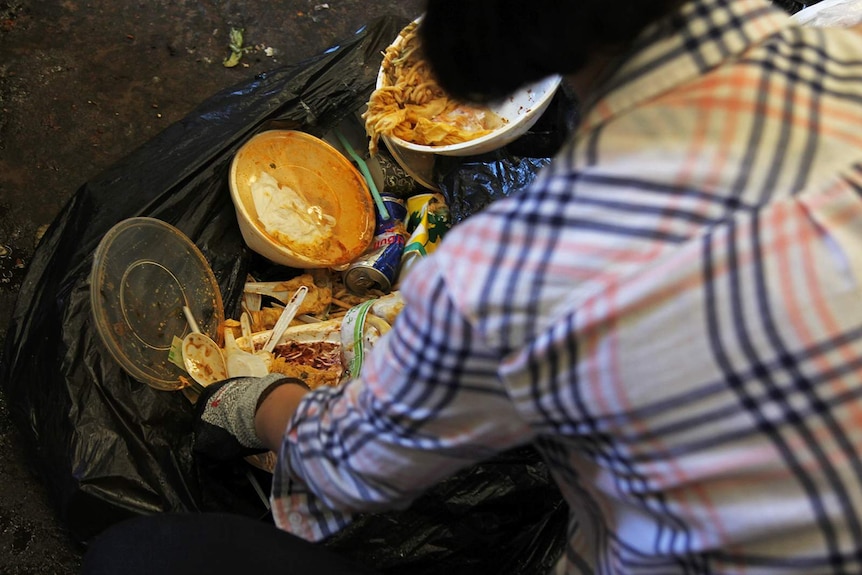 A volunteer at the waste facility digs into a garbage bag containing plastic containers filed with food stuffs.
