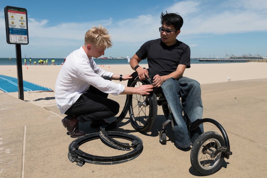 Ryan Tilley bends down and fits the Gecko Traxx to Huy Nguyen's wheelchair.