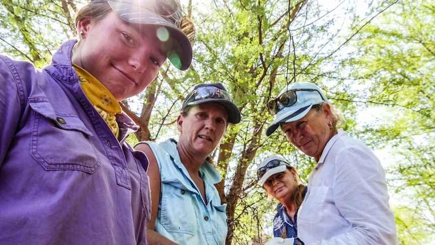 Four women stand along a fence line and take a break for a photo.