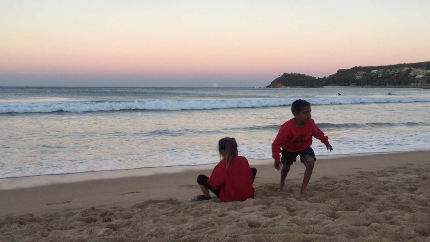 Children watching a pink sunset and moonrise over the ocean.