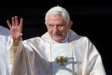 Pope Benedict waves to a crowd while wearing a white cap and white robes.