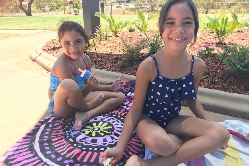 Temperance Armstrong, 6, and her sister Aurelia, 8, sit sit on towels in the shade at the Mount Isa local pool.