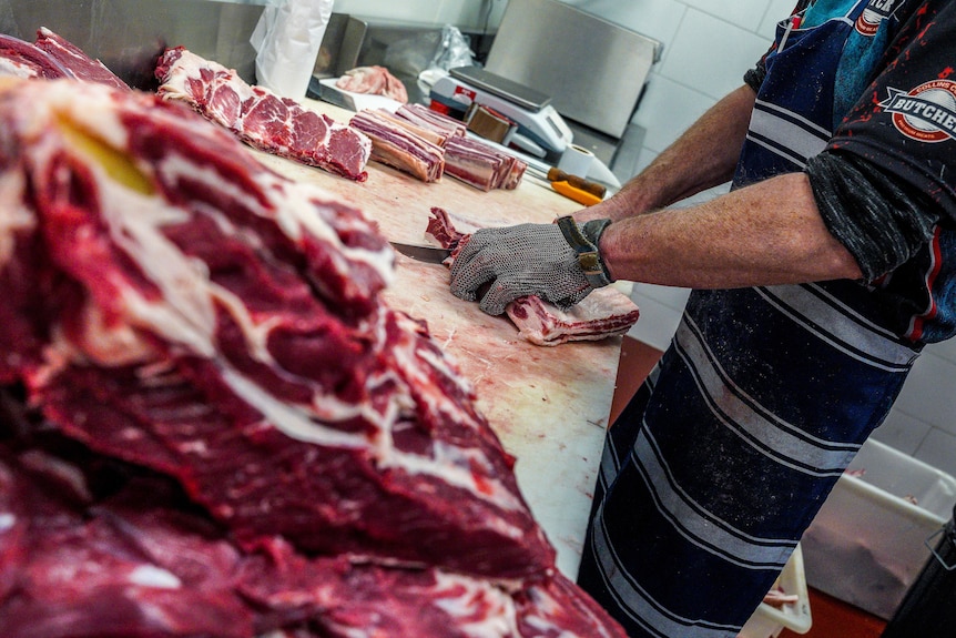 Butcher slices through beef with beef piled high in foreground