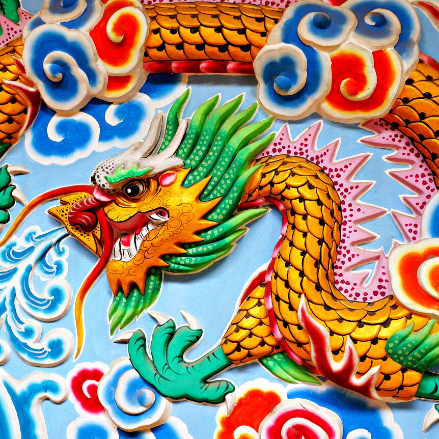 a carving of a bright and colourful dragon and fish on a wall with pale blue background