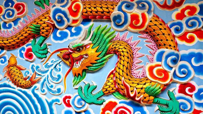 a carving of a bright and colourful dragon and fish on a wall with pale blue background