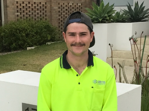 Zac smiles and stands in front of a mailbox.