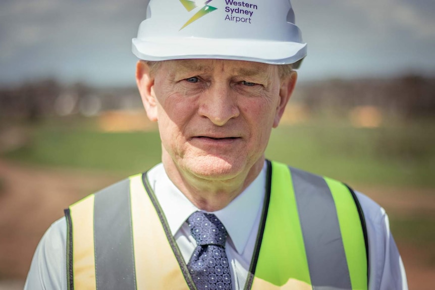 A man wearing a hard hat and high-vis vest looks into the camera.