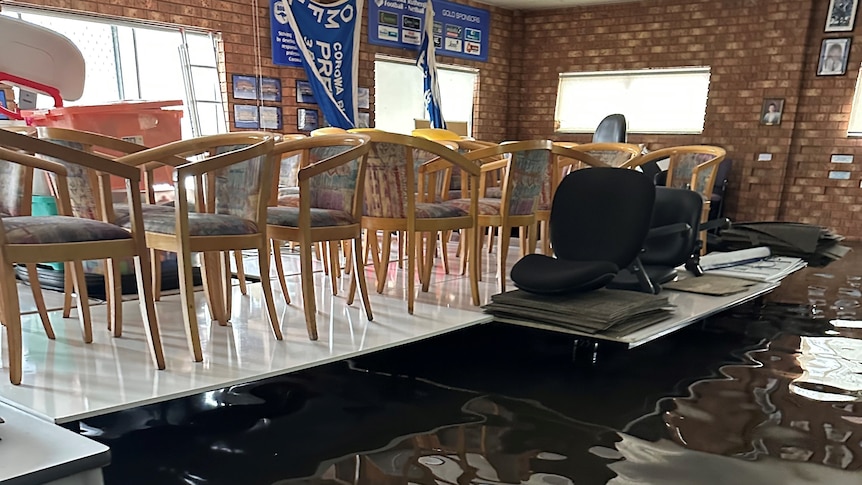 A brick footy clubroom during a flood, with water coming up to the table legs. Chairs are on top of the table