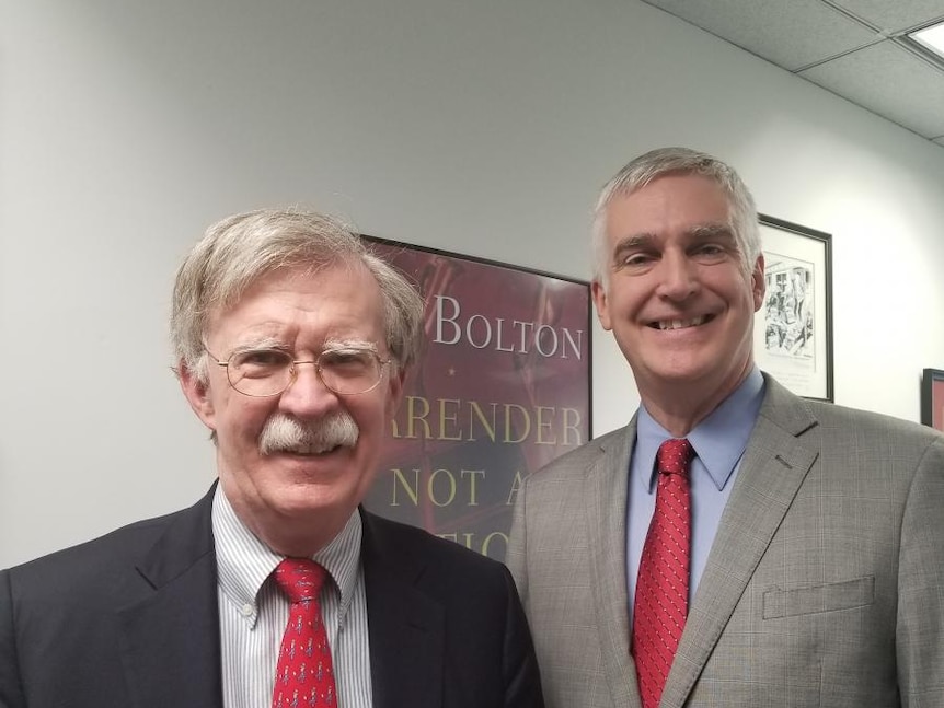 John Bolton, left, smiling and wearing a black suit, with Fred Fleitz, left, smiling and wearing a grey suit.