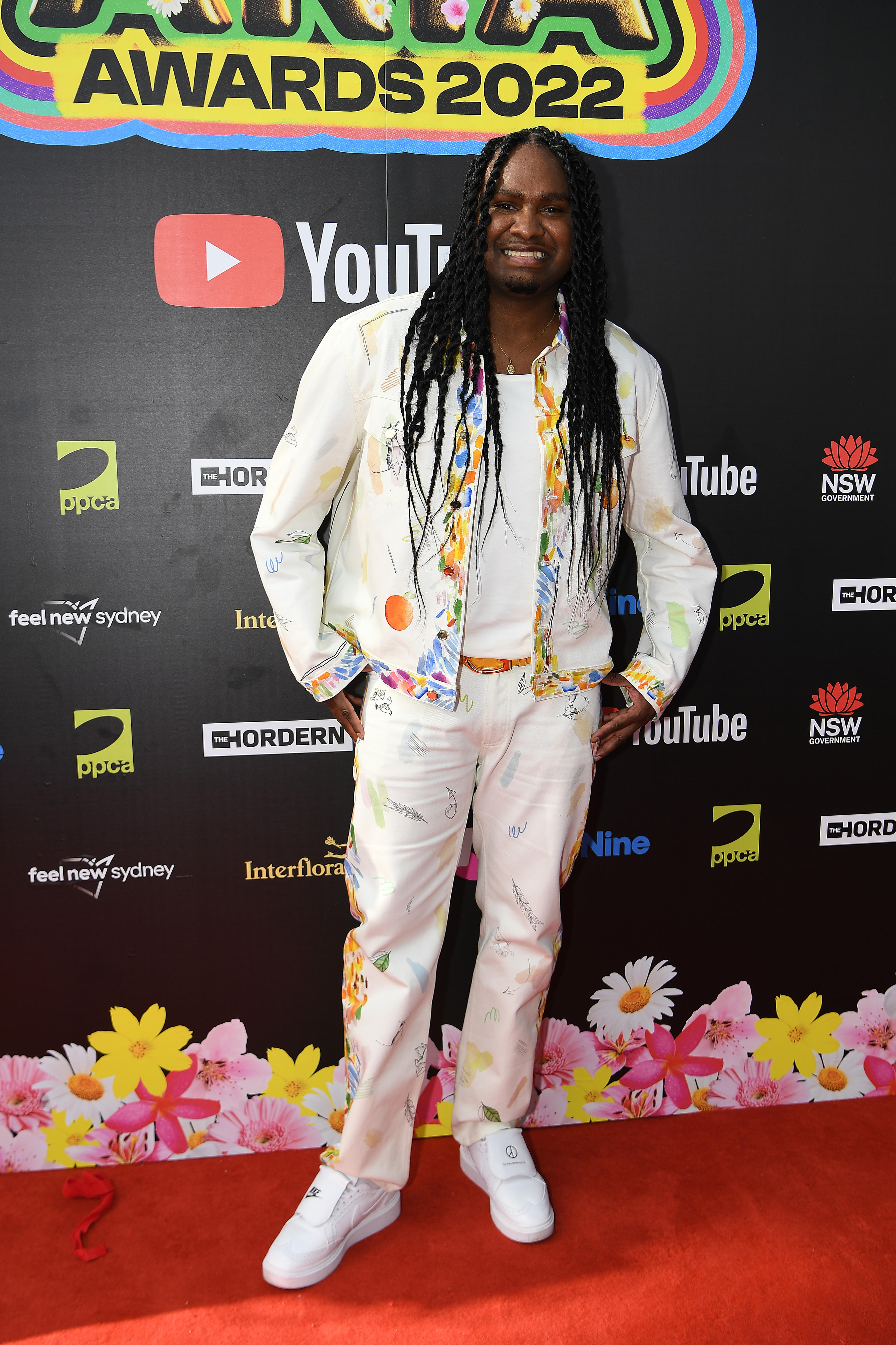 Baker Boy wears a white suit with colorful details on the sides.