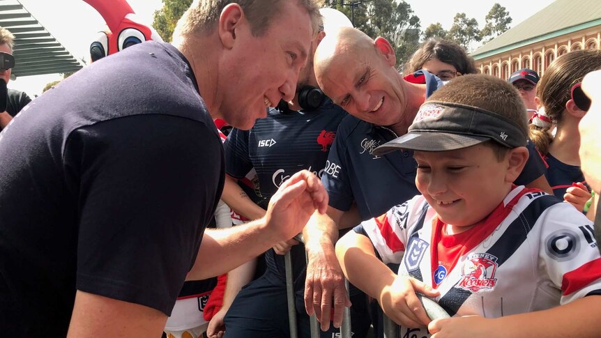 A man speaks to a young boy wearing a Sydney Roosters jersey.