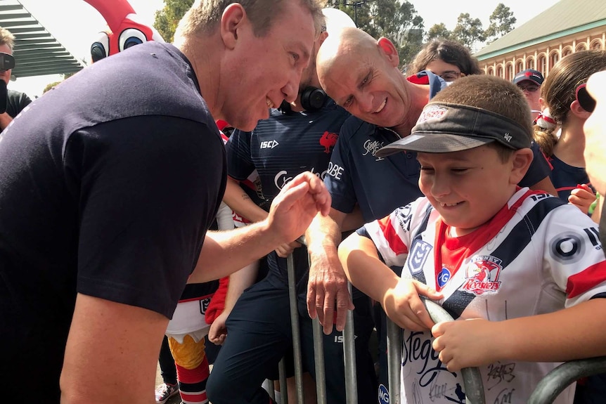 A man speaks to a young boy wearing a Sydney Roosters jersey.
