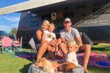A family sitting in front of a caravan smiling.