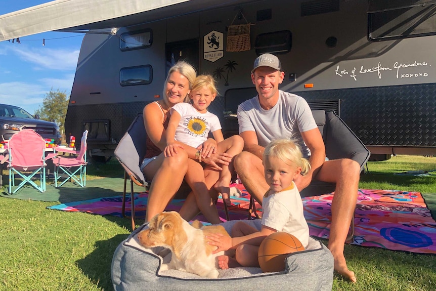 A family sitting in front of a caravan smiling.