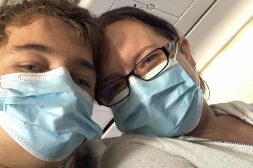 A selfie of a woman and teenage boy in a plane with masks on