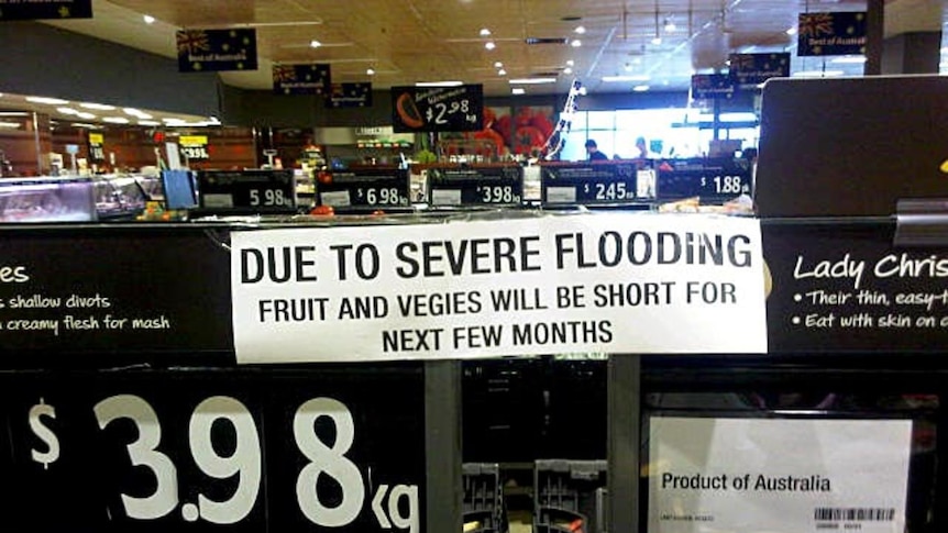 A sign sits on a fruit and vege shelf in a Woolworths supermarket