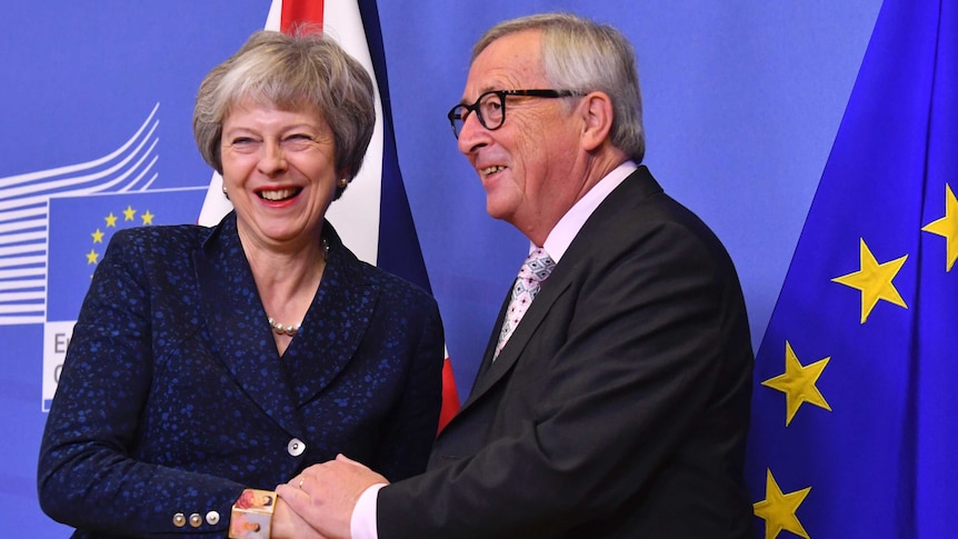 A smiling Theresa May and Jean-Claude Juncker shake hands