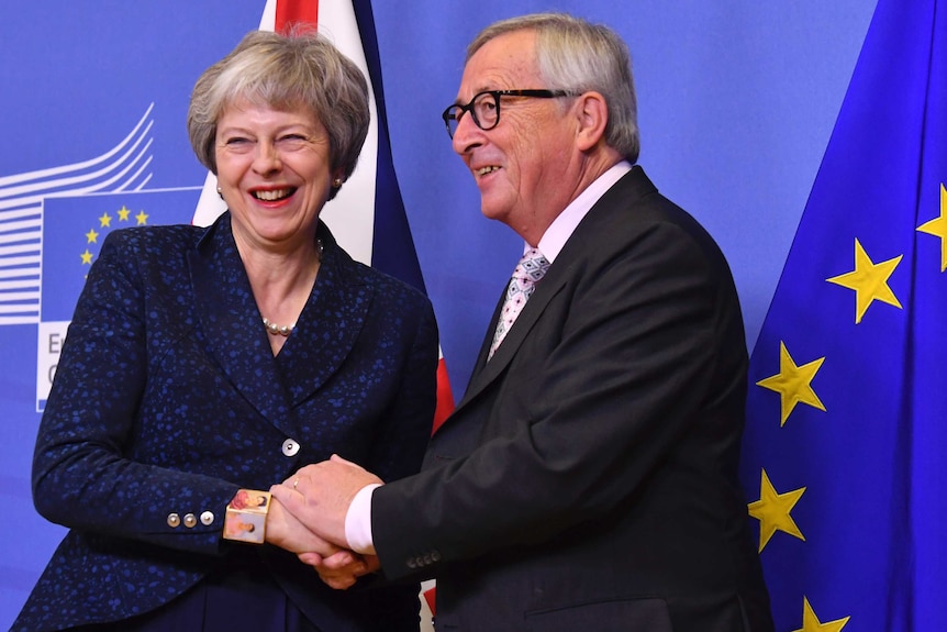 A smiling Theresa May and Jean-Claude Juncker shake hands