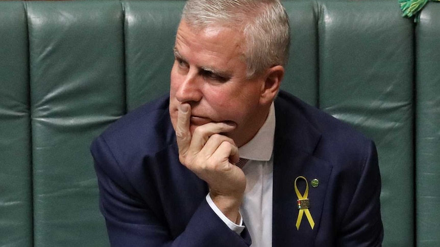 McCormack sits alone looking to the left of frame with right hand on chin and pointer finger raised to his mouth.