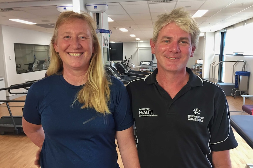 A woman and man smile. He is wearing a shirt with a University of Canberra health faculty logo on it.