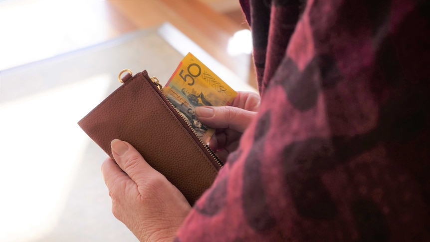 A woman wearing a headscarf holds a $ 50 bill.