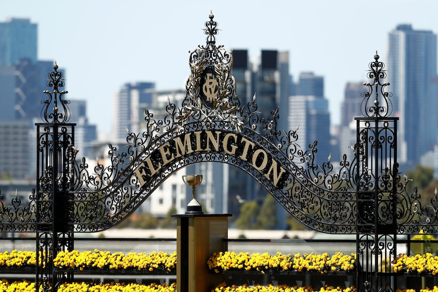 A photo of the finishing post at Flemington racecourse, with wrought metal gates, a sign saying 'Flemington' and a trophy.