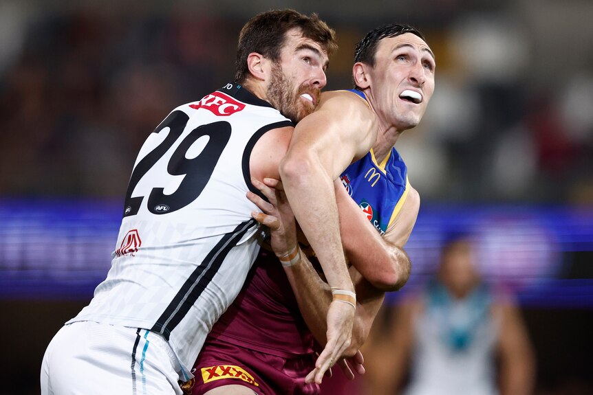 Two ruckmen wrestle as they look up towards the ball during an AFL game.