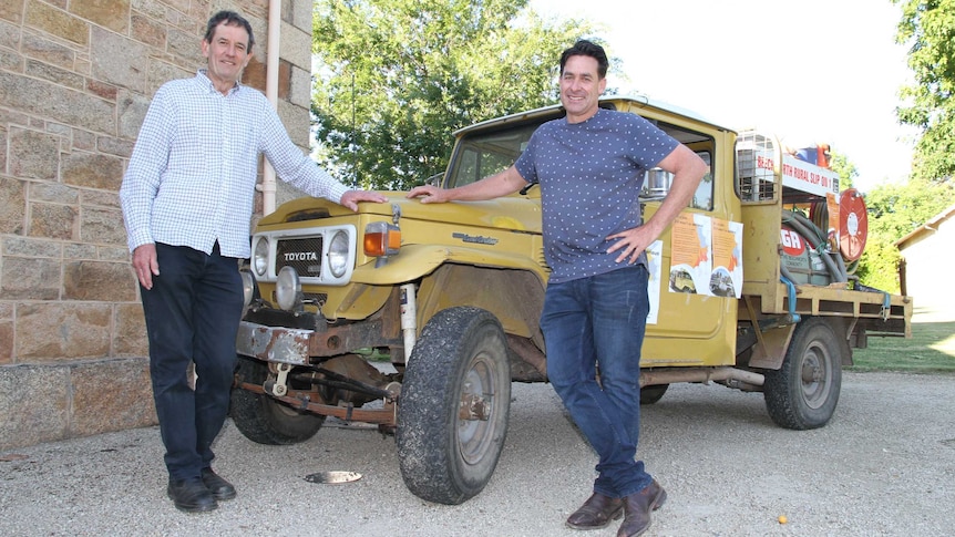 two men stand next to 40 year old vehicle