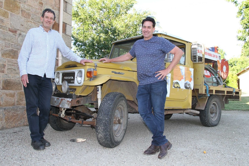 two men stand next to 40 year old vehicle