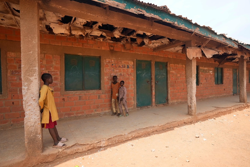 Three Nigerian school children leaning on a building.